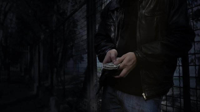 Man counts fake money in dark park alley at night.