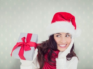 Composite image of surprised brunette in santa hat holding gift