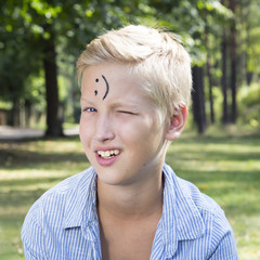 Winking boy sits on green grass in forest. Concept of happy thou