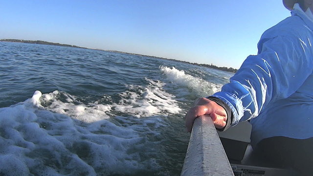 View from the stern of a dinghy with wake from outboard motor with hand on boat gunwale.