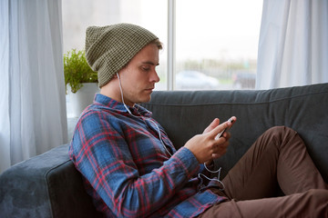 Young guy on his couch listening to music on his phone