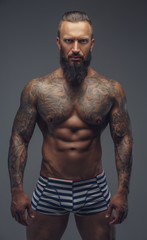 Tattooed muscular man with beard in stripes panties.