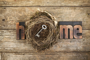 Home, word written with letterpress printing blocks and bird nest with key on rustic wood