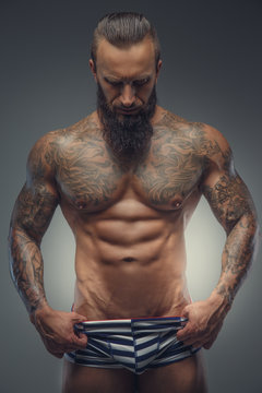 Tattooed muscular man with beard in stripes panties.