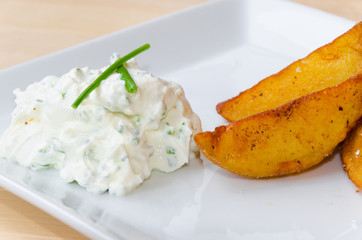 Creamy dip with herbs and fried potatoes on white plate lying on wooden background