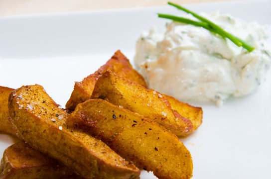 Fried potatoes on white plate with creamy dip