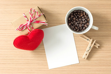 Top view of paper or cardboard, clothes pegs, red heart, gift box and coffee bean in coffee cup on wooden background. Lots of copy space for your idea.