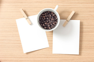 Top view of paper or cardboard with clothes pegs and coffee bean in coffee cup on wooden background. Lots of copy space for your idea.