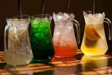 Multicolored soft drinks, lemonade in jugs. Wooden table background