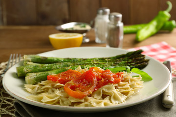 Roasted asparagus and tasty pasta with vegetables on plate on wooden table background