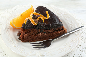 Piece of Chocolate cake and orange on plate, on table  background