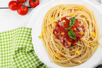 Spaghetti with tomato sauce and cheese on white plate, on color wooden background