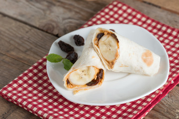 Slice tortilla wrap with peanut butter, raisin and banana on whi