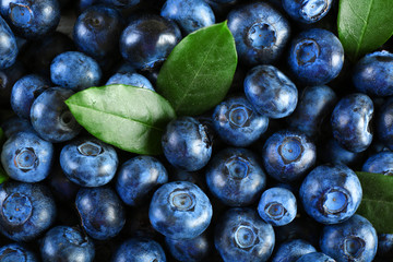 Tasty ripe blueberries with green leaves close up