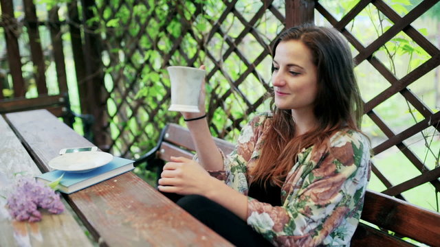 Girl drinking coffee in the arbour and smiling to the camera
