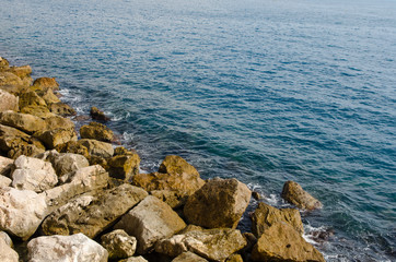 Fototapeta na wymiar waves of the mediterranean sea water crushing into reddish rocks of the shore