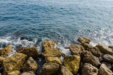 top view of waves of the mediterranean sea water crushing into reddish rocks of the shore