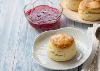 Freshly baked homemade scone with raspberry jam on a white plate, selective focus