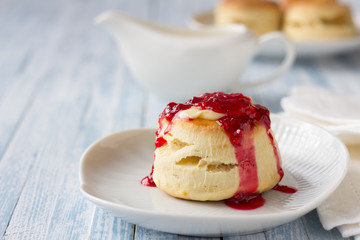 Freshly baked homemade scone with raspberry jam on a white plate, selective focus