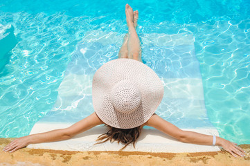Woman in big whire hat relaxing on the swimming pool