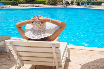 Woman in a big white hat relaxing on a lounger by the pool