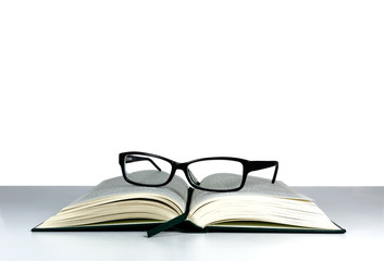 Book and reading glasses on a white table and white background