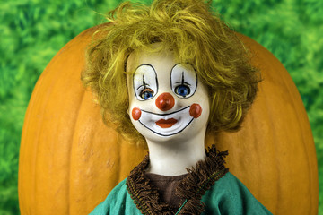 antique porcelain clown doll  in front of orange pumpkin on green background