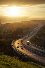 Asphalt highway with electronic toll gate in autumn woodland at sunset. The bridge spanning the...