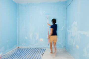 Motion blur woman painting wall in blue.