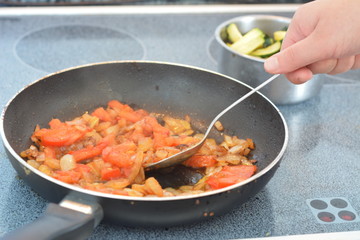 Рука мешает овощи на сковороде.