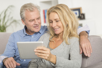 Mature couple sitting in sofa and using tablet pc