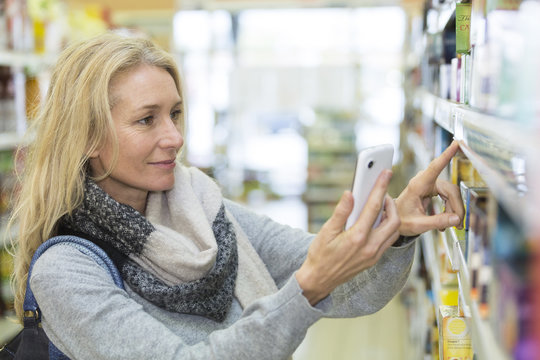Mature woman comparing the price of tea with mobil phone