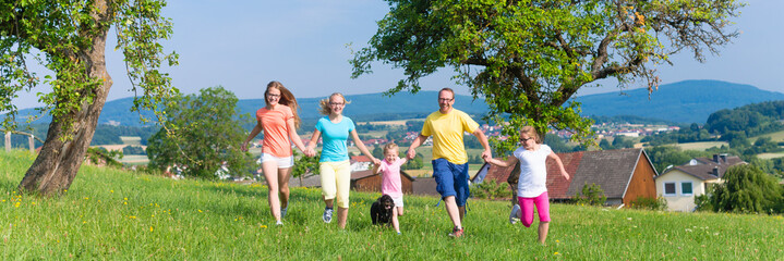Vater mit Kindern rennt über grüne Wiese im Gras