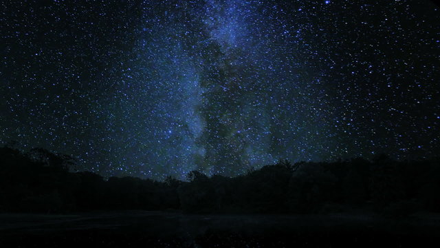 Milkway Spin Over Trees. the beautiful milky way spins over top silhouetted trees. reflected in lake below.

