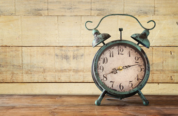 image of vintage alarm clock on wooden table in front of wooden background. retro filtered

