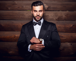 Portrait of young beautiful fashionable man against wooden wall In black suit & bow tie.
