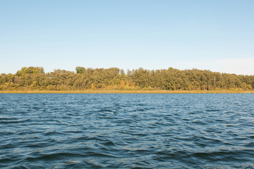 Landscape with view of lakeside and autumn  forest under blue sky.