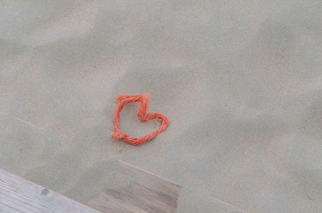 Ein rotes Seil in Herzform im Sand.