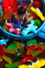 colorful jelly candies in the shape of a worm and a spider in a large cup on brown wooden background closeup