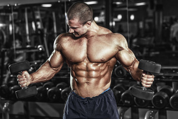 Fototapeta na wymiar Athlete muscular bodybuilder in the gym training biceps with dumbbells