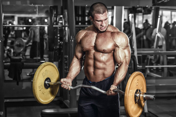 Fototapeta na wymiar Athlete muscular bodybuilder in the gym training biceps with bar