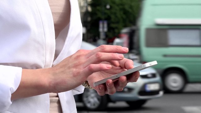 young attractive blonde woman works on smartphone - urban street with cars in the city - closeup