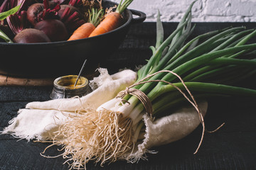 Green onions, carrots, beets, salt on textiles on a black wooden background