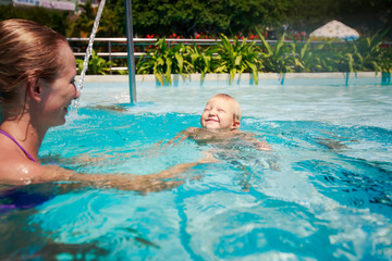 closeup mother looks at small girl swimming in hotel pool