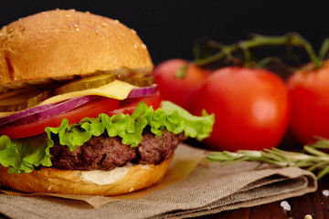Big juicy beef burger on background tomatoes and herbs