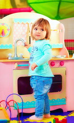 cute little girl playing with toy kitchen in kindergarten