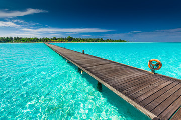 Fototapeta na wymiar Long wooden jetty over atoll and a tropical island in Maldives