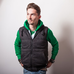 Emotional portrait of attractive young man in a grey vest & green sweater with a hood. Studio...