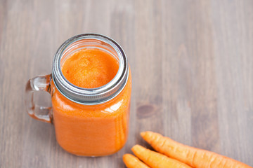 A carrot smoothie in a jar with carrots on wooden background