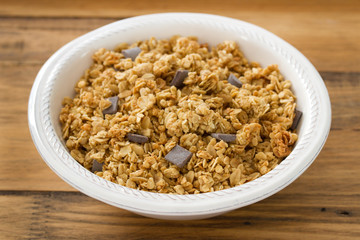 granola with chocolate on white bowl on brown wooden background